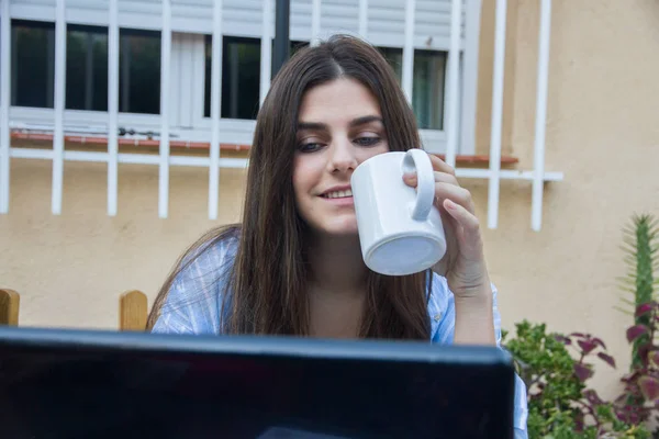 Jeune femme d'affaires aux yeux bleus buvant du café tout en travaillant avec un ordinateur portable . — Photo