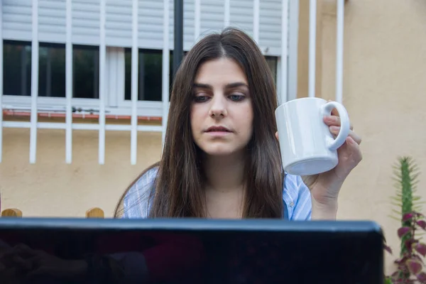 Jeune femme d'affaires aux yeux bleus buvant du café tout en travaillant avec un ordinateur portable . — Photo