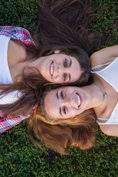 Mujeres amigas tumbadas boca arriba en el césped de un parque. Son felices y disfrutan de un hermoso día . — Foto de Stock