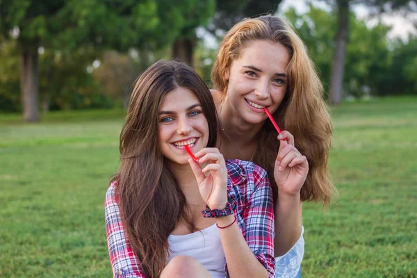 Amigas disfrutando mientras comen regaliz rojo unas vacaciones en el parque . — Foto de Stock
