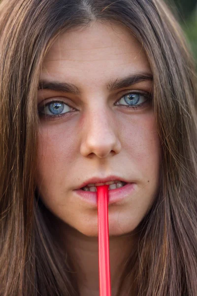 Menina com olhos azuis e cabelo castanho comendo alcaçuz vermelho. Retrato foto é um close-up de seu rosto . — Fotografia de Stock
