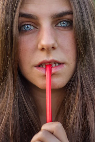 Chica joven con ojos azules y cabello castaño comiendo regaliz rojo. Foto de retrato es un primer plano de su cara . — Foto de Stock