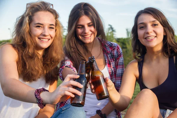 Amigas comemorando o feriado se divertindo bebendo cerveja em um parque. Estão a brindar com garrafas. . — Fotografia de Stock