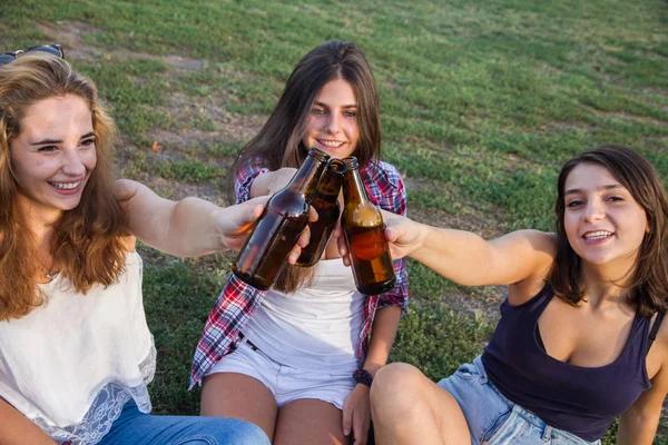 Amigas comemorando o feriado se divertindo bebendo cerveja em um parque. Estão a brindar com garrafas. . — Fotografia de Stock