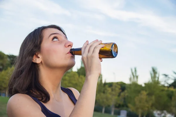 Muito jovem morena bebendo de uma garrafa de cerveja no parque . — Fotografia de Stock