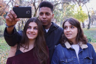 Bir grup genç insan, iki beyaz kız ve siyah bir erkek çocuk alanında bir cep telefonu ile bir selfie yapıyor.