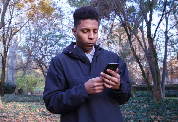 Homem negro enviando mensagens com seu smartphone no campo . — Fotografia de Stock