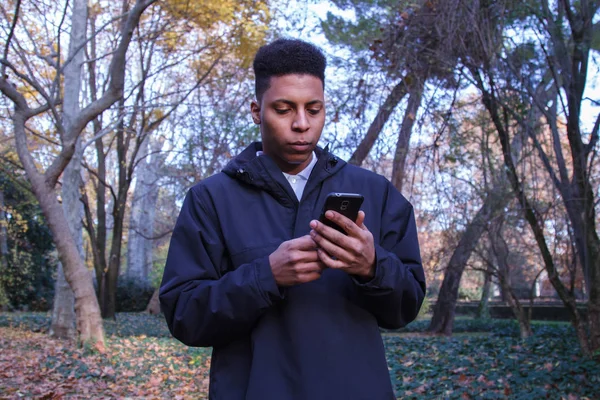 Чорний чоловік надсилає повідомлення зі смартфоном у полі . — стокове фото