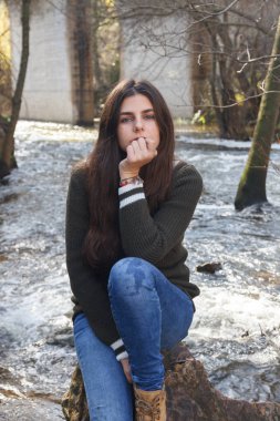 Dağda bir nehir kıyısında bir kayaya oturan mavi gözlü genç kız. 