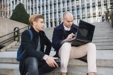 İki genç girişimci, bir kel ve sarı saçlı bir dizüstü bilgisayar ve akıllı telefon şehrin bazı merdivenlerde çalışma ile diğer. 