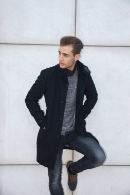 Genç modern yakışıklı sarışın mavi gözlü poz beyaz duvara yaslanmış, kamera seyir, bir ceket giyen işadamı.