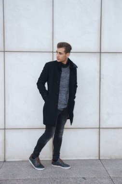 Genç modern yakışıklı sarışın mavi gözlü poz beyaz duvara yaslanmış, kamera seyir, bir ceket giyen işadamı.