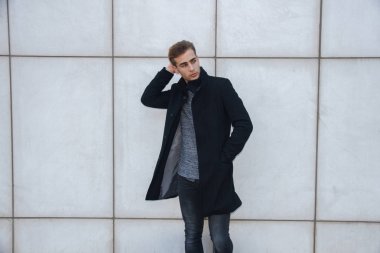 Genç modern yakışıklı sarışın mavi gözlü poz beyaz duvara yaslanmış, kamera seyir, bir ceket giyen işadamı.