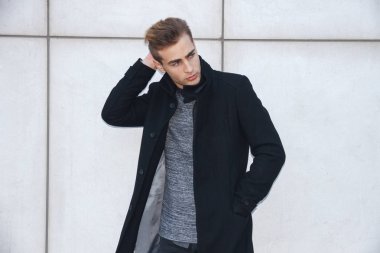 Genç modern yakışıklı sarışın mavi gözlü poz beyaz duvara yaslanmış, kamera seyir, bir ceket giyen işadamı.