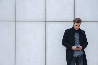 Bir akıllı telefon tutarak genç yakışıklı sarışın iş adamı. Beyaz duvara yaslanmış telefonla sohbet. 
