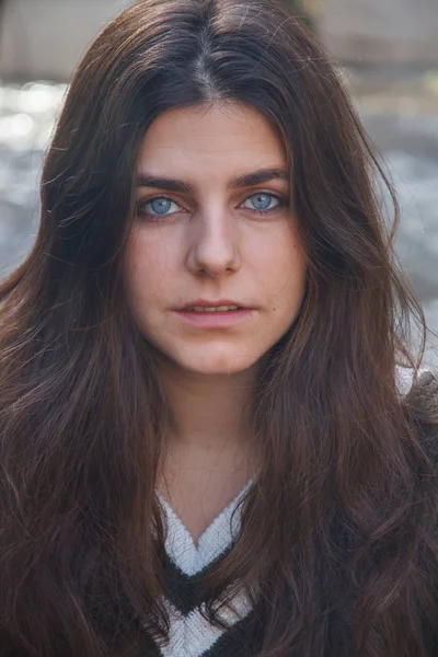 Portret van een jong meisje met blauwe ogen, zittend op een rots aan de oever van een rivier in de bergen. — Stockfoto