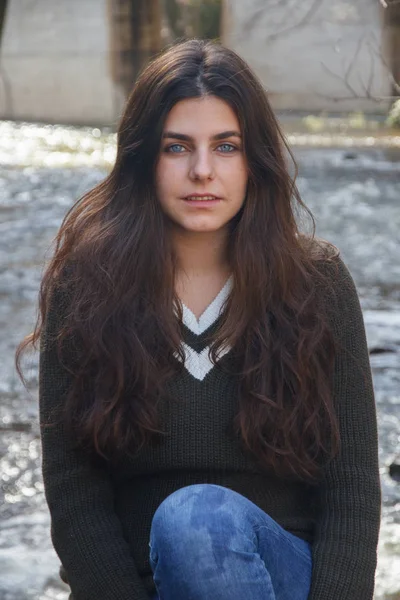 Portret van een jong meisje met blauwe ogen, zittend op een rots aan de oever van een rivier in de bergen. — Stockfoto