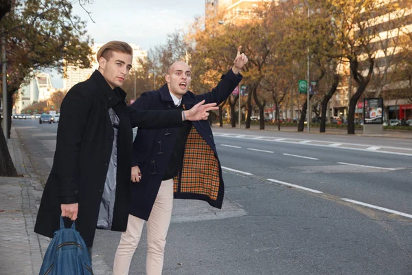 Two young handsome caucasian businessmen outdoor in the city, one of them nail and the other with brown hair, asking for a taxi.