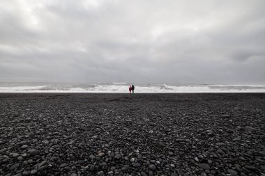 İki tanınmayan insanlar bir siyah kum plajı üzerinde denizde seyir 