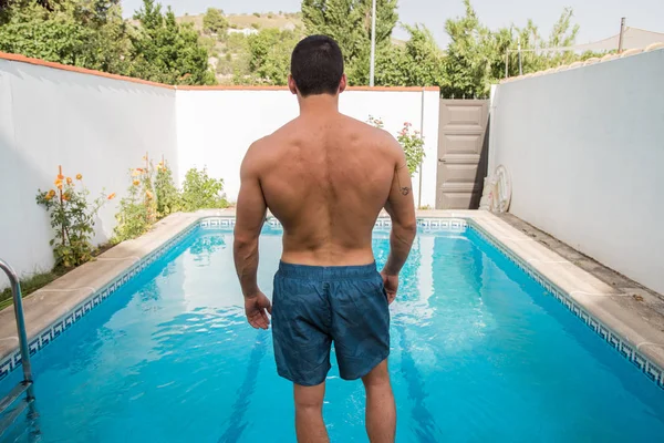 Güneşli bir günde havuz kenarında ayakta güçlü genç adam.