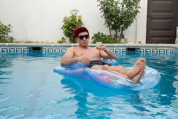 Mladý muž silné pití piva na nafukovací postel v bazénu — Stock fotografie