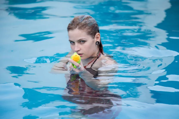 Mooie Kaukasische meisje met blauwe ogen schiet met een waterpistool in het zwembad. — Stockfoto