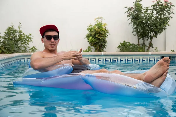Ung stark man dricka öl på en luftmadrass i poolen — Stockfoto