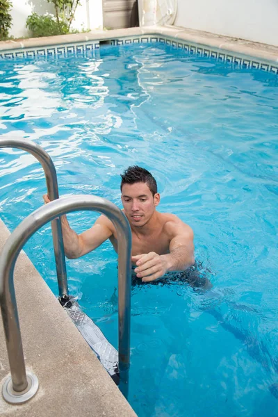 Junger starker Mann steigt die Treppe des Pools hinauf, um rauszukommen. — Stockfoto