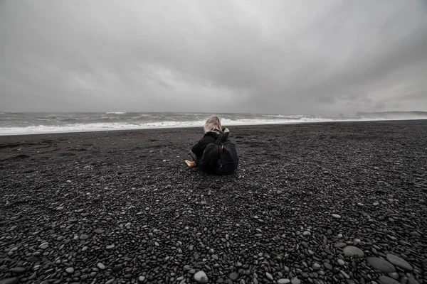 Siyah Kum Plajı üzerinde oturan genç bir kadın arkadan görünüm