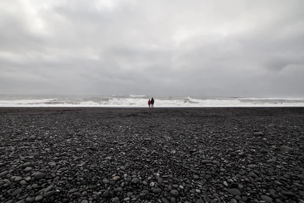 İki tanınmayan insanlar bir siyah kum plajı üzerinde denizde seyir 