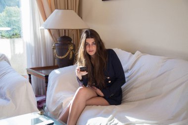 Genç ve güzel beyaz esmer kız evinin oturma odasında televizyon izlerken mavi gözlü. Uzaktan kumandayla kanal geçiş yapıyor. 