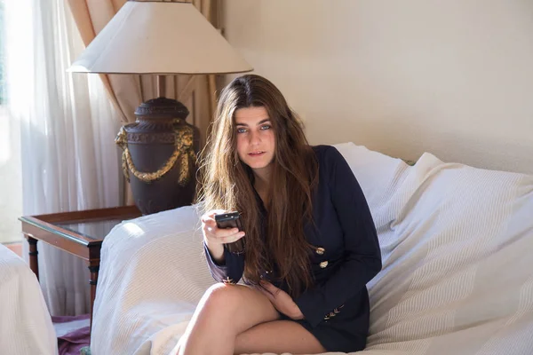 Genç ve güzel beyaz esmer kız evinin oturma odasında televizyon izlerken mavi gözlü. Uzaktan kumandayla kanal geçiş yapıyor. 