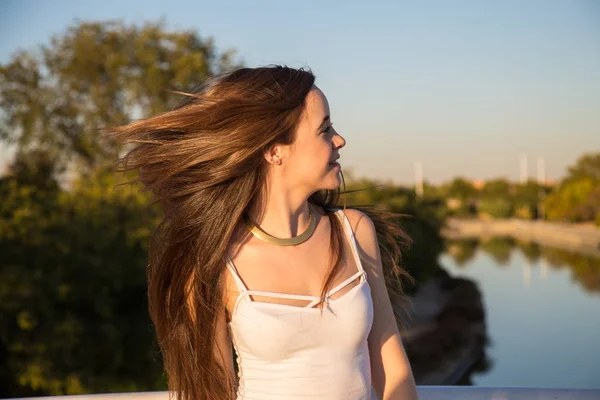 美丽的年轻女子在阳光明媚的公园里在人工河的背景下晃动头发 — 图库照片