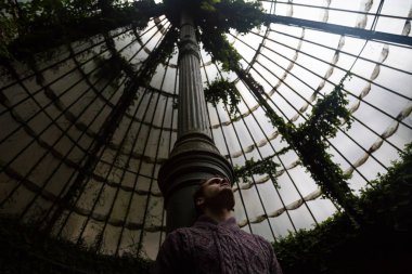 Genç adam bir sera Botanik Bahçe sütununda yaslanmış.