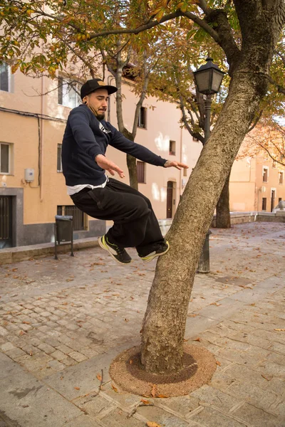 Young man doing an amazing parkour trick on a tree in the street.