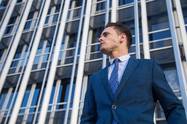 Portrait of stylish man in elegant suit posing confidently on background of modern office skyscraper.