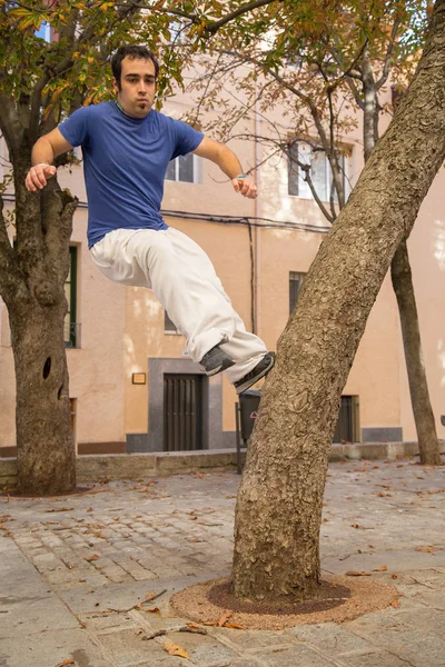 Young man doing an amazing parkour trick on a tree in the street.