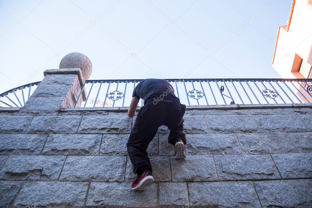 Young man hanging on wall and trying to climb up while doing parkour. 