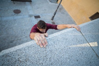 Ellerini duvarda asılı ve parkour yaparken yukarı tırmanmaya çalışan genç adam.