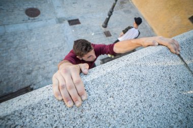 Ellerini duvarda asılı ve parkour yaparken yukarı tırmanmaya çalışan genç adam.