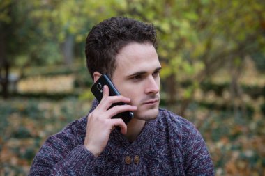 Genç yakışıklı adam ile yeşillik çayır üzerinde oturan ve smartphone ile iletişim.