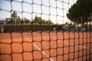 Öğleden sonra üzerinden net görülen sahada oynayan profesyonel tenis oyuncu adam. 