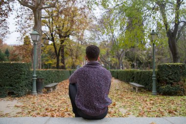 Sonbahar Park merdivenlerde oturan ve uzağa bakarak düşünceli genç adam. 