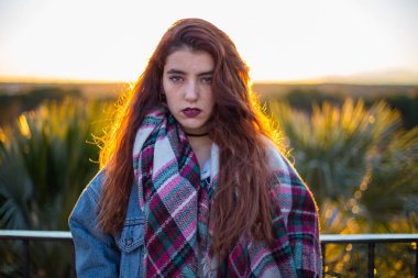 Trendy denim ceket ve arkada doğa üzerinde yaktı kamera alluringly bakarak eşarp genç esmer. 