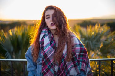 Trendy denim ceket ve arkada doğa üzerinde yaktı kamera alluringly bakarak eşarp genç esmer. 