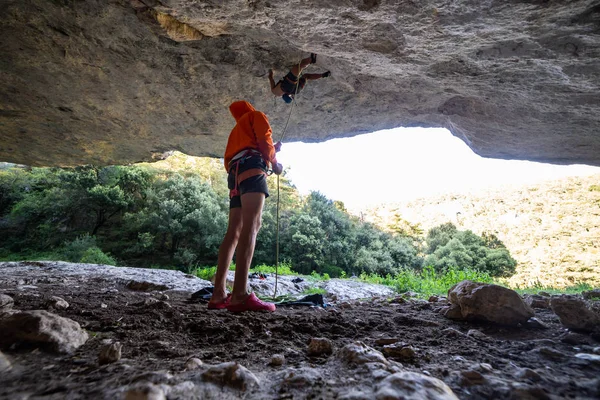 ロープを保持し 自然を背景に仲間の登山岩の屋根を確保若い男の下から — ストック写真