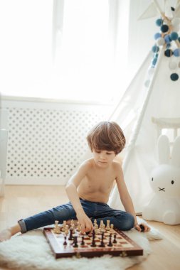 Genç bir çocuk yerde satranç oynuyor. Parlak oda güneşli bir gün. Satranç tahtası. Konsantre olmayı öğreniyorum..