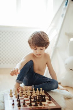 Genç bir çocuk yerde satranç oynuyor. Parlak oda güneşli bir gün. Satranç tahtası. Konsantre olmayı öğreniyorum..