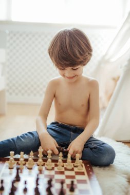 Genç bir çocuk yerde satranç oynuyor. Parlak oda güneşli bir gün. Satranç tahtası. Konsantre olmayı öğreniyorum..