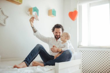 Oyuncak uçakla oynayan bir çocuğun genç babası. Mutlu bir aile, güneşli bir odada birlikte yatakta vakit geçiren iki erkek..
